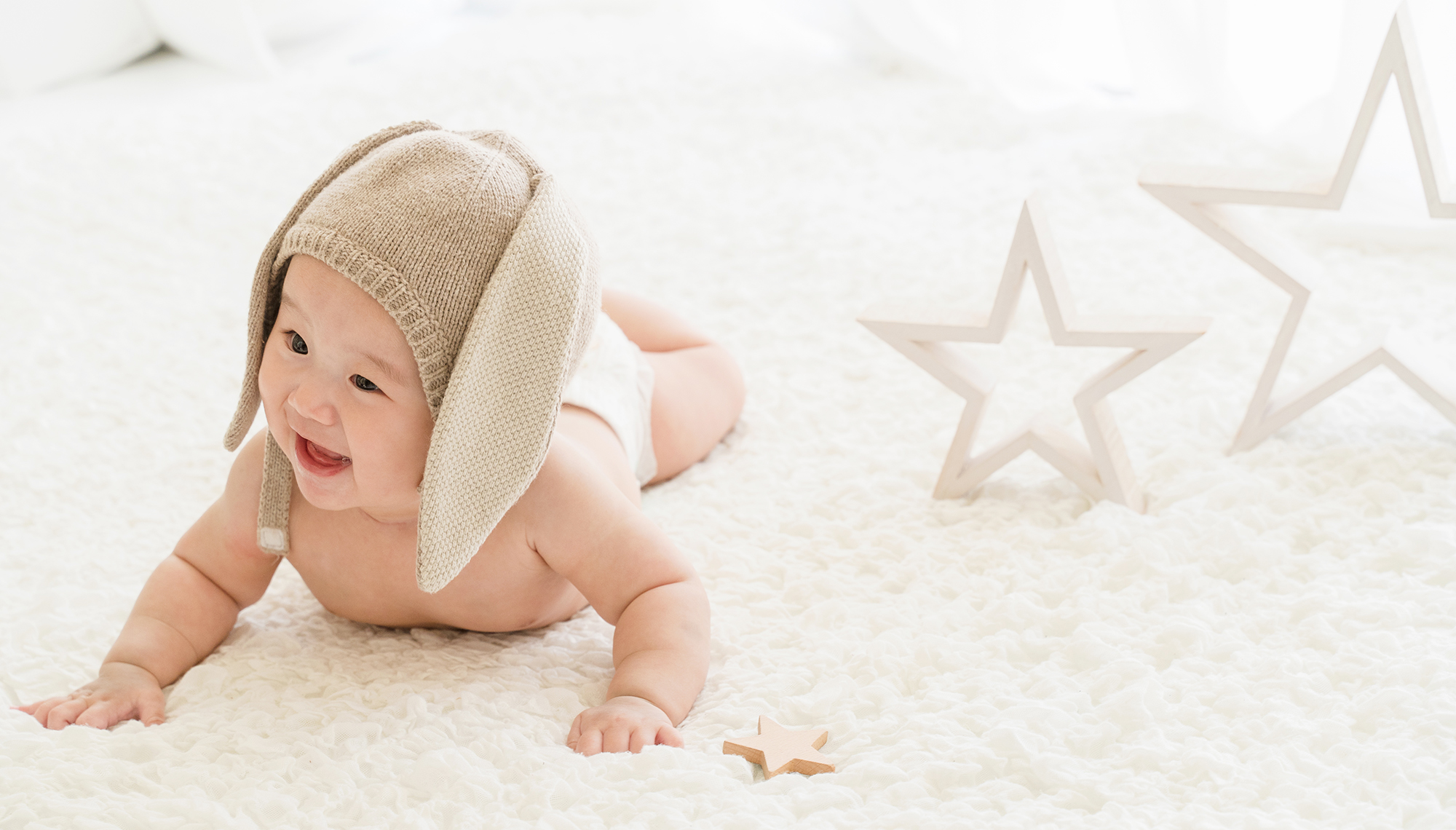 白のカーペットを上をウサギ耳の帽子とおむつをした赤ちゃんがはいはい歩きしている写真