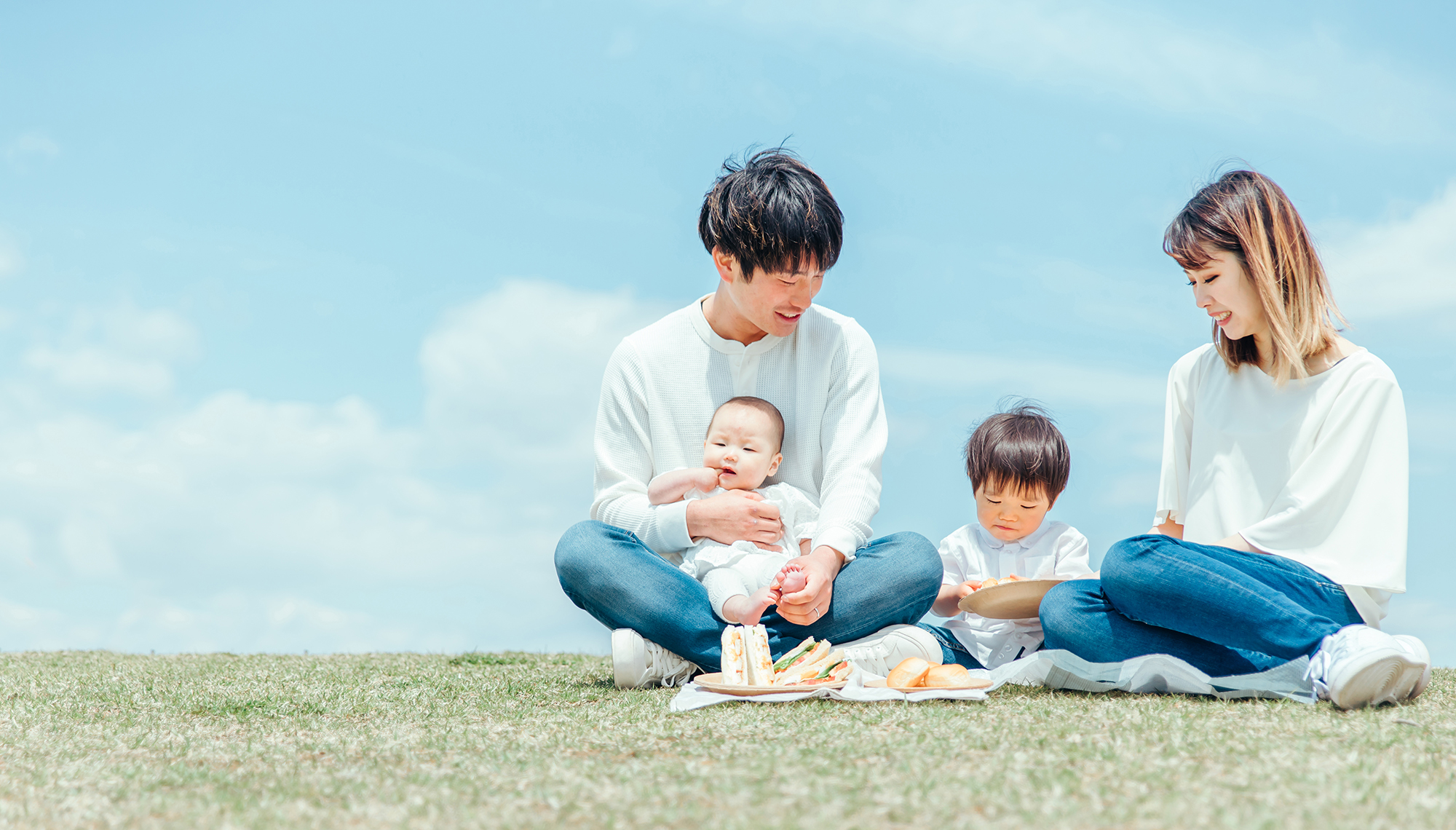 公園の芝生に家族4人で座ってサンドイッチを食べている写真