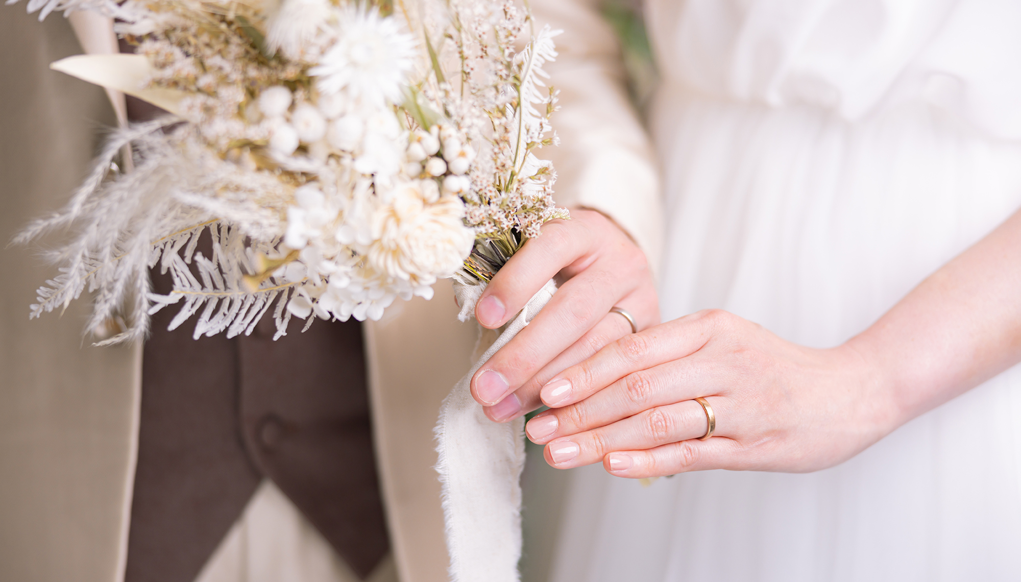 ウェディングドレス姿の女性とタキシードを着た男性が結婚指輪をした手元が写った写真
